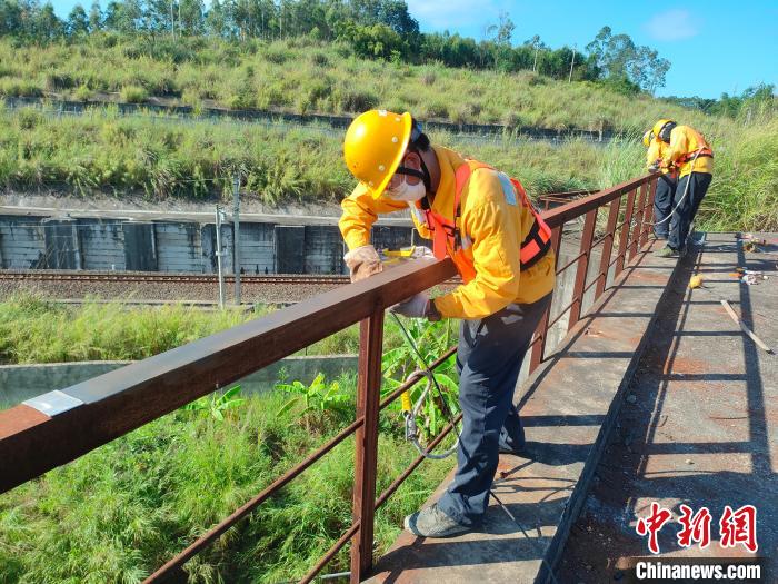 圖為高溫下南寧工務(wù)段橋梁工全副武裝對鐵路橋梁人行道欄桿打磨除銹?！●T博 攝